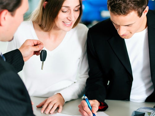 Couple singing papers at sales desk, salesman handing them a car key