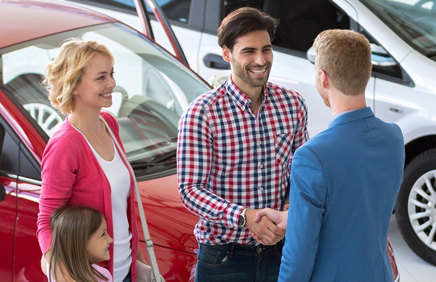 Family talking to salesman in car dealership, men shaking hands