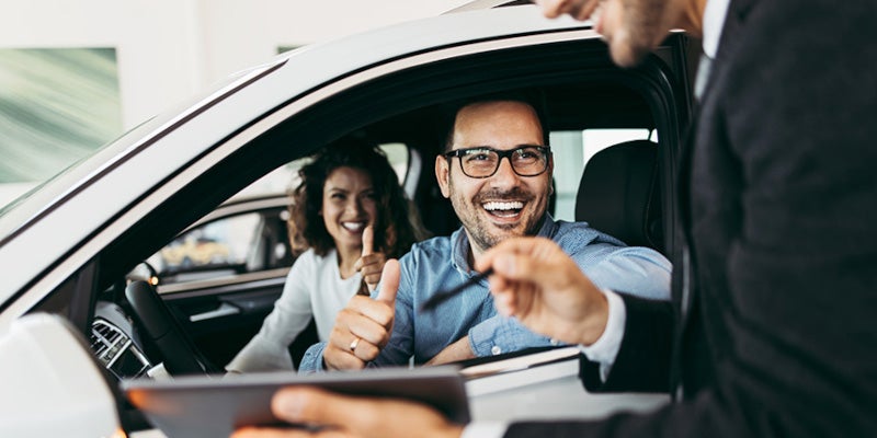 Couple in car smiling talking to sales manager 