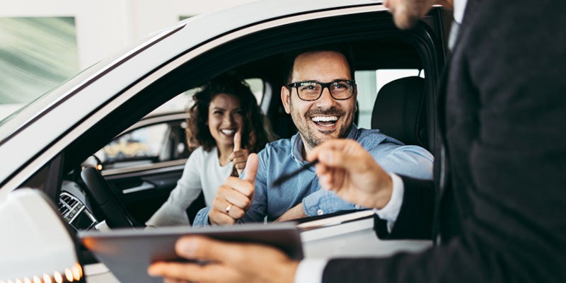 Couple in car smiling talking to salesman through the window