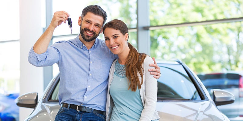 Smiling couple standing in front of new car holding up keys
