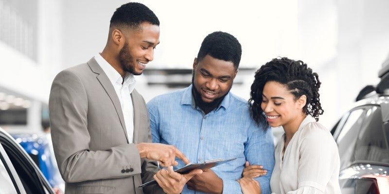 Car salesman speaking to couple in dealership showroom