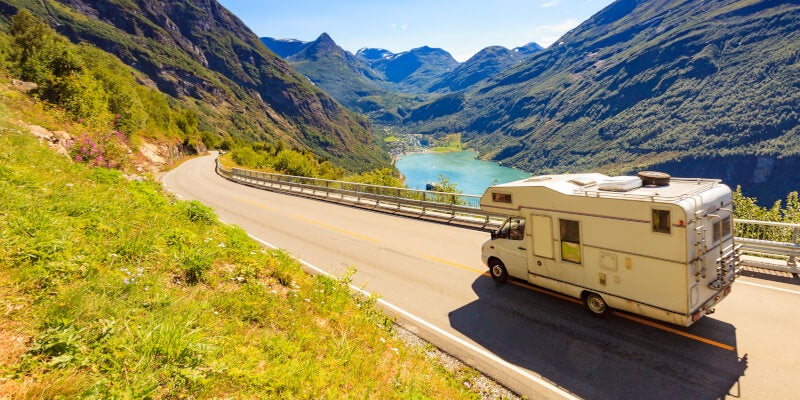 A RV driving on a road overlooking mountains and a lake