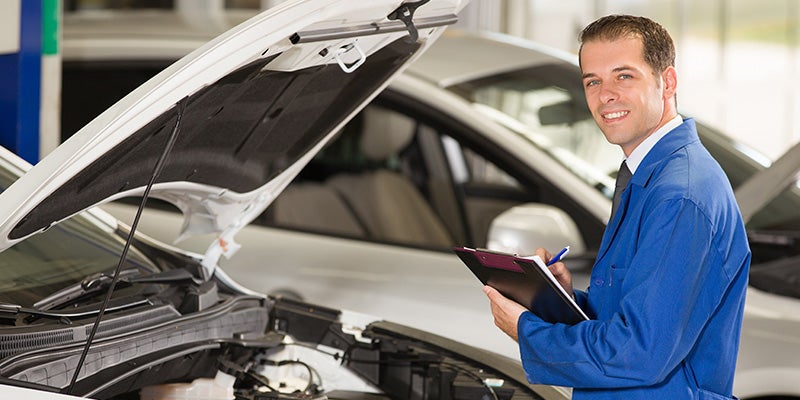 Mechanic holding clipboard looking at car engine